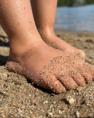 Lapsen varpaat kesäisen järven hiekkarannalla.