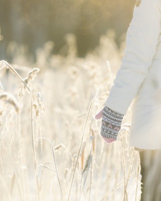 Ulkovaatteisiin pukeutunut aikuinen seisoo selin talvisessa peltomaisemassa. Aurinko paistaa. 
