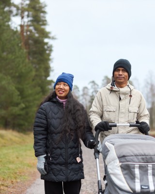 Pariskunta ulkoiluttamassa vauvaa rattaissa.