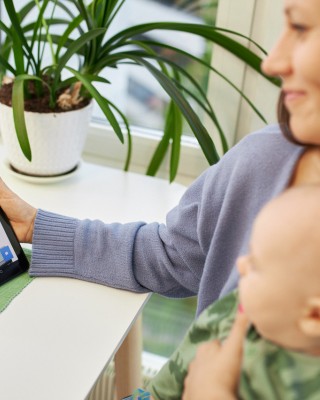 Henkilö katsoo mobiililaitetta vauva sylissään