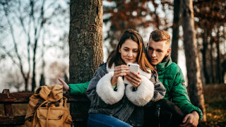 Nuori nainen ja mies luonnossa katsovat kännykkää.