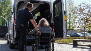 Asiakas on pyörätuolissa ja kuljettaja avustaa. Kuvaaja Anni Äikäs.