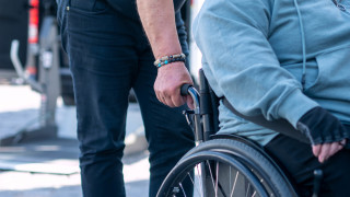 Ihminen pyörätuolissa jota toinen ihminen työntää.