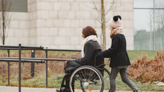 Avustaja työntää pyörätuolissa olevaa naista.