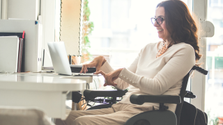 Nainen pyörätuolissa käyttää tietokonetta.