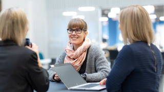 Kolme henkilöä keskustelevat tietokoneiden ääressä.