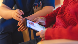 Kotihoidon ammattilainen näyttää ikäääntyneelle miten käytetään etähoivan tablettia.