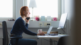 Nainen puhuu puhelimessa ja istuu työkoneen äärellä.
