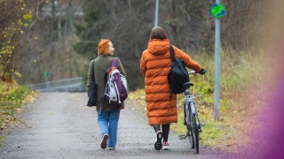 Nainen taluttaa pyörää ystävän kanssa syysmaisemassa.