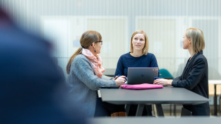 Kolme henkilöä istuvat pöydä ääressä.