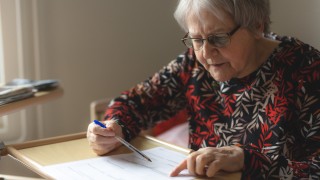 Iäkäs henkilö täyttää lomaketta.