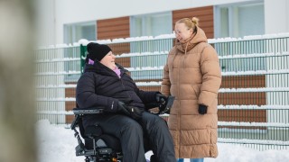 Henkilö pyörätuolissa ja hänen avustajansa.