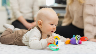Vauva pötköttää vatsallaan lattialla ja leikkii värikkäillä leluilla.