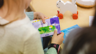 Lapsi katsoo kuvakortteja. Kuvassa lapsen olkapää ja kädet.