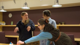 Villasukkakilpailun raatiin kuuluvat Tuire Selin ja Kati Kallimo keskustelevat kilpailutöistä. Kristiina Lempiäinen-Trzaska kurottaa pöydän yli sujauttamaan pisteytyslapun yhdelle kilpailutyölle.