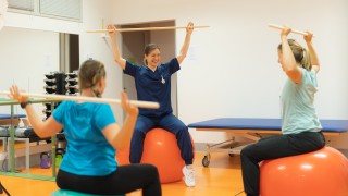 Kolme ihmistä istuu jumppapalloilla ja tekee keppijumppaa.