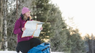 Nainen ulkoilemassa talvella, katsoo karttaa metsän reunalla.