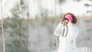 Nainen tähystää kiikareilla talvisäässä.