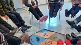 Ihmiset istuvat piirissä jalat ylhäällä, keskellä on pelilauta.