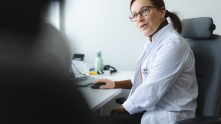 Lääkäri istuu tuolissa tietokoneen ääressä katse kohti asiakasta.