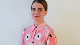 Henkilö seisoo kasvot kohti kameraa hymyillen.