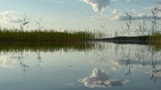 Aurinkoinen järvimaisema, jossa pilvet heijastuvat vedenpinnasta