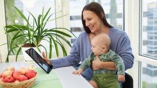 Aikuinen vauva sylissään. Katsovat tablet-tietokonetta.