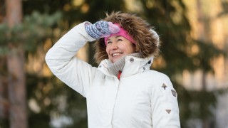 Nainen tähyilee iloisesti kaukaisuuteen talvivaatteissa.