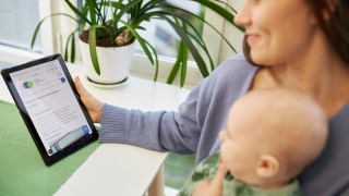 Nainen tablettitietokone kädessä ja vauva sylissä