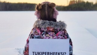 Lapsi istuu lumessa selin kameraan ja lapussa lukee Tukiperheeksi?