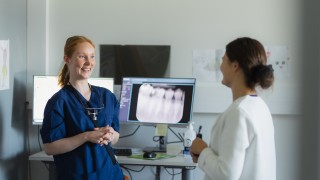 Kaksi suun terveydenhuollon ammattilaista keskustelevat hymyillen työpisteen ääressä.