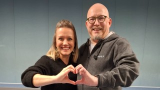 Nainen ja mies katsovat iloisesti kameraan ja muodostavat käsillään sydämen.