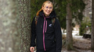 Nainen seisoo ulkona iloisena puun vieressä. 