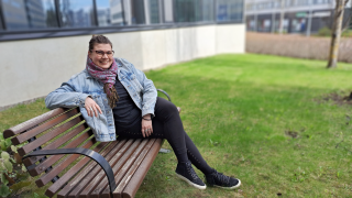 Nainen istuu penkillä ja katsoo hymyillen kameraan.