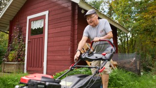 Mies käynnistää ruohonleikkuria kotipihalla.