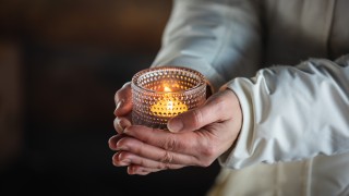 Henkilö kannattelee tuikkukynttilää käsissään. 