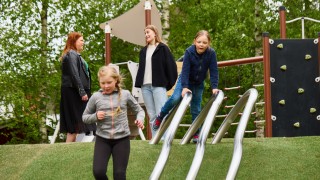 Lapsia ja aikuisia puuhaamassa vehreässä leikkipuistossa.