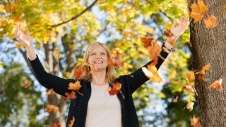 Nainen heittää syksyn ruskan lehtiä ilmaan.