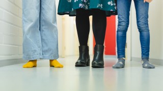 Kolme henkilöä seisoo rivissä sisätiloissa, näkyvissä vain jalat ja lattia.