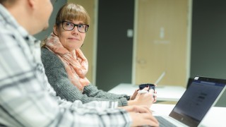 Kaksi työntekijää ovat tietokoneen ääressä ja katsovat toisiaan hymyillen.