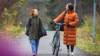 Kaksi naista kävelevät syksyisellä kadulla ja katsovat toisiinsa.