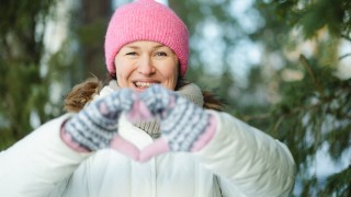 Nainen ulkona tekee lapaset kädessä sormistaan sydämen.