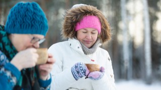 Kaksi naista juo hymyillen kuksasta talvisessa maisemassa.