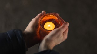 Kaksi kättä pitää tuikkukippoa, jossa palaa lämmin tuikku.