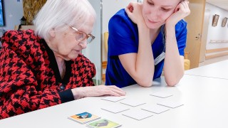 Ikääntynyt ja opiskelija pelaavat muistipeliä.