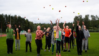 Koululaiset heittävät palloja ilmaan urheilukentällä