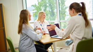 Kolme työntekijää keskustelee iloisesti pöydän ympärillä.