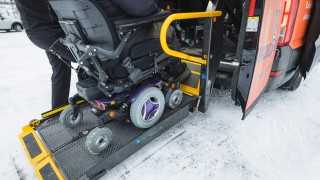 Pyörätuolissa istuva henkilö ja taksi.