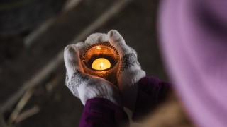 Henkilö pitää käsissään lämpökynttilää lasiastiassa