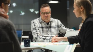 Kolme henkilöä istuu pöydän ääressä. Pöydällä on karttakuva Keski-Suomesta, jota yksi osoittaa sormellaan.